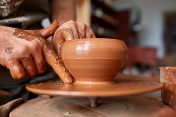 Fototapeta na wymiar Close-up hands of a male potter in apron making a vase from clay, selective focus