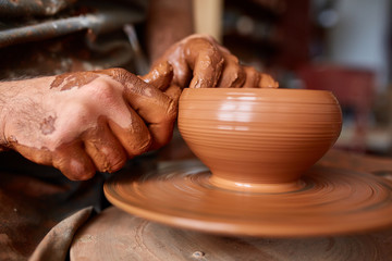 Fototapeta na wymiar Close-up hands of a male potter in apron making a vase from clay, selective focus
