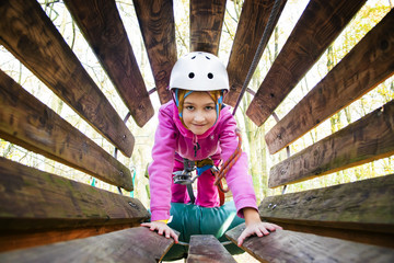 Young girl in harness climbing through a barrel in an adventure park.