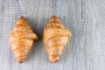 Two croissant are placed on a gray wooden table