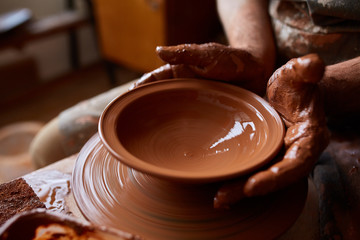 Close-up hands of a male potter in apron making a vase from clay, selective focus