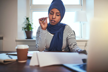 Young Arabic female entrepreneur reading documents in her home o