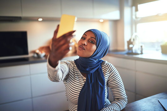 Smiling Arabic woman making faces while taking selfies at home