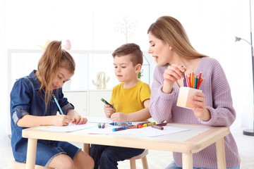 Cute little children and their nanny drawing at home