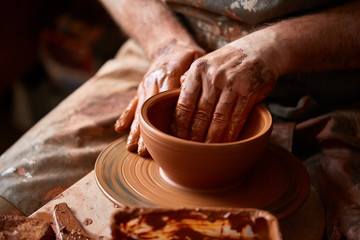 Close-up hands of a male potter in apron making a vase from clay, selective focus