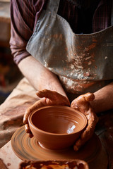 Portrait of a male potter in apron molds bowl from clay, selective focus, close-up