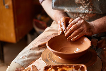 Close-up hands of a male potter in apron making a vase from clay, selective focus