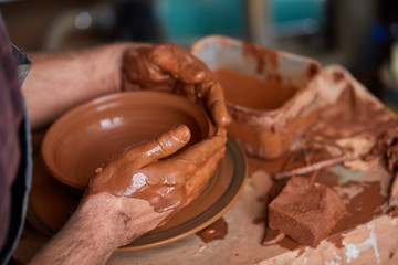 Close-up hands of a male potter in apron making a vase from clay, selective focus