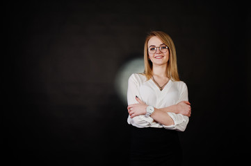 Studio portrait of blonde businesswoman in glasses, white blouse and black skirt against dark background. Successful woman and stylish girl concept.