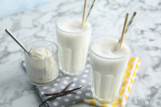 Glasses with milk shake and tasty vanilla ice cream on light background