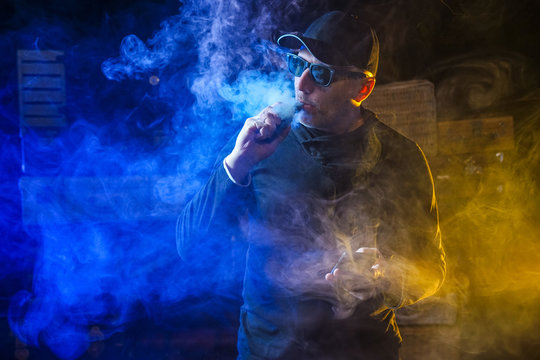 Vape man.  A man lets out steam from an electronic cigarette. An alternative to cigarettes. A man smokes electronic cigarettes. vaping man holding a mod.