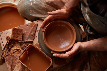 Close-up hands of a male potter in apron making a vase from clay, selective focus