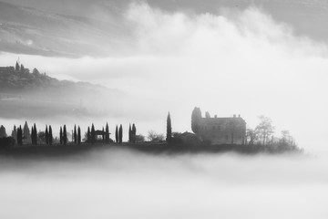 Beautiful foggy sunrise in Tuscany, Italy with cypresses and house. Natural misty background in black and white