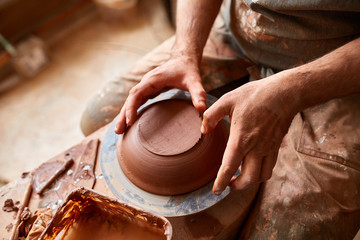 Close-up hands of a male potter in apron making a vase from clay, selective focus