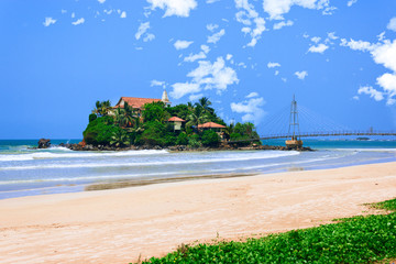 Buddhist island temple in Matara on Pigeon Island. Blue clean sky. Old crossing bridge at the Parey dewa temple with green trees.