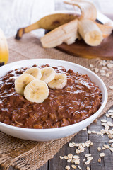 Chocolate oatmeal for breakfast with slices of a ripe banana in a white bowl on a wooden background in a horizontal position.