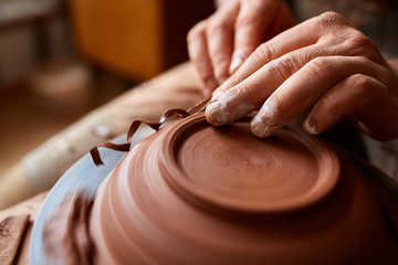 Close-up hands of a male potter in apron making a vase from clay, selective focus