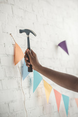 cropped image of man nailing up string with party garland on brick wall