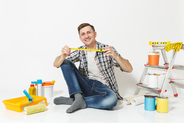 Man in casual clothes sitting on floor with measure tape, instruments for renovation apartment room isolated on white background. Wallpaper, gluing accessories, painting tools. Repair home concept.