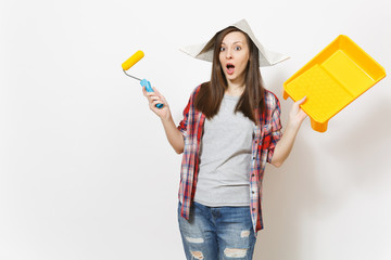 Young shocked beautiful woman in newspaper hat holding roller for wall painting and paint tray isolated on white background. Instruments, tools for renovation apartment room. Repair home concept.