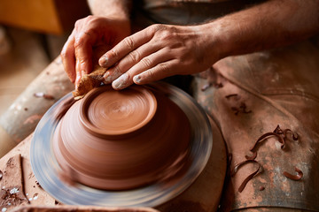 Close-up hands of a male potter in apron making a vase from clay, selective focus
