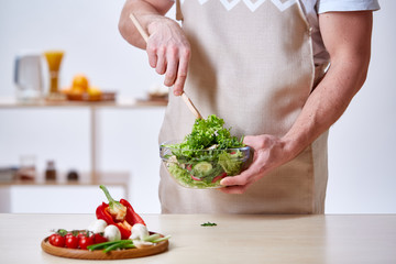 Man cooking at kitchen making healthy vegetable salad, close-up, selective focus.