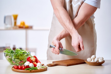 Man cooking at kitchen making healthy vegetable salad, close-up, selective focus.