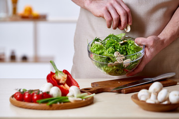 Man cooking at kitchen making healthy vegetable salad, close-up, selective focus.