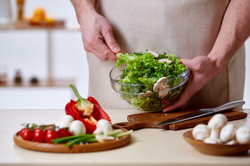 Man cooking at kitchen making healthy vegetable salad, close-up, selective focus.