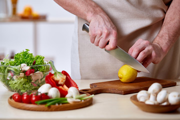Man cooking at kitchen making healthy vegetable salad, close-up, selective focus.