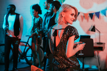 Blonde woman holding glass with cocktail by friends at party