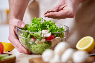 Naklejka na ściany i meble Man cooking at kitchen making healthy vegetable salad, close-up, selective focus.