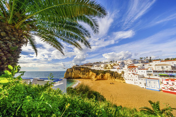 Obraz premium Sandy beach surrounded by cliffs with palm trees in Carvoeiro, Algarve, Portugal