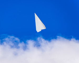 White paper airplane in a blue sky with clouds. The message symbol in the messenger