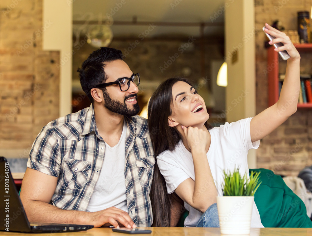 Wall mural Two students, bearded man and brunette girl taking selfie with smartphone in modern coworking office