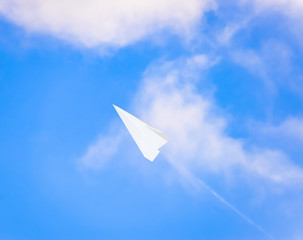 Fototapeta na wymiar White paper airplane in a blue sky with clouds. The message symbol in the messenger