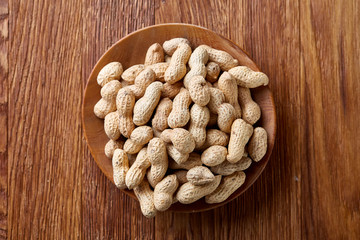 Unpeeled peanuts in wooden bowl over rustic wooden background closeup, selective focus