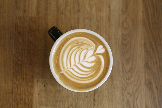 Artisanal Latte with Delicate Rosetta Art on a Warm Wooden Table, Overhead View