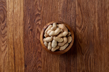 Unpeeled peanuts in wooden bowl over rustic wooden background closeup, selective focus