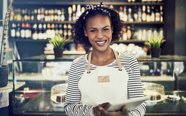 Smiling entrepreneur standing in her cafe using a digital tablet