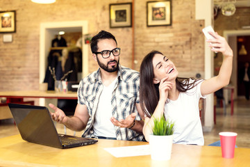 Couple of colleagues, bearded man and brunette girl taking selfie with smartphone in modern coworking office