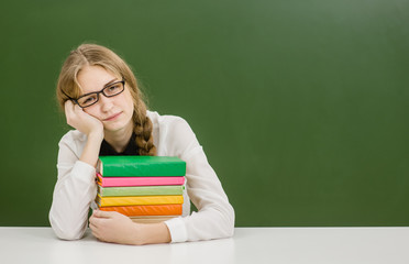 Tired teen girl with books on the background of a school board looking at camera. Space for text