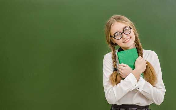 Smiling nerd student girl  with book on the background of a school board. Space for text