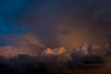 Stroke of lightning with storm clouds and golden sunset light