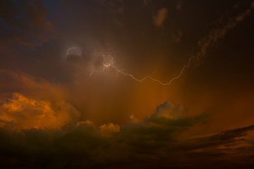 Stroke of lightning with storm clouds and golden sunset light