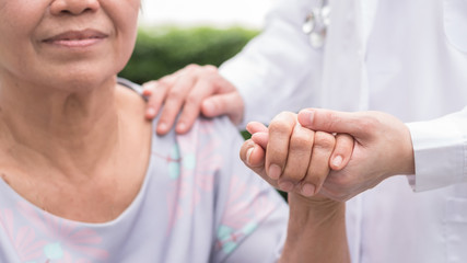 Elderly senior patient in nursing home holding doctor's hand having happy health check, medical...
