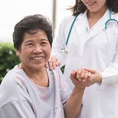 Elderly senior patient in nursing home holding doctor's hand having happy health check-up, medical...