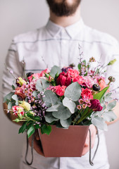 Very nice attractive young man holding a basket of fresh blossoming flowers, cropped vertical photo