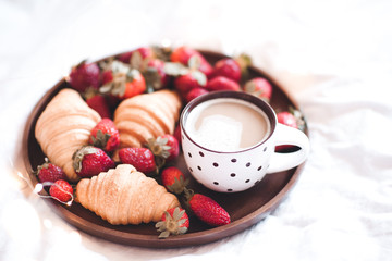Cup of coffee with strawberry croissants on tray in bed closeup. Good morning.