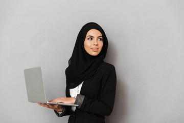 Portrait of muslim elegant woman 20s in black traditional clothing smiling and looking aside on...